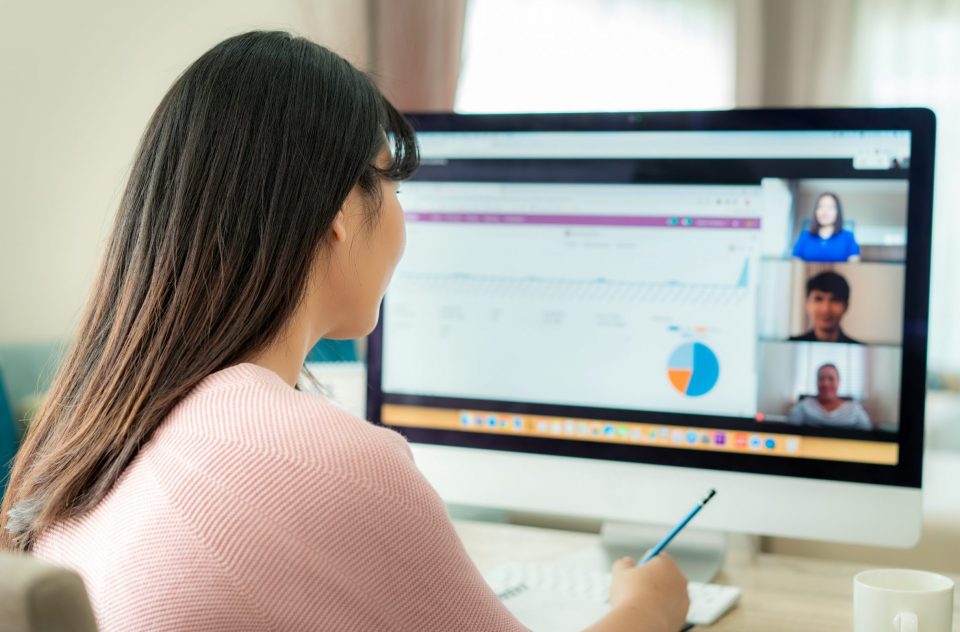 Back view of Asian business woman talking to her colleagues about plan in video conference. Multiethnic business team using computer for a online meeting in video call. Group of people smart working from home. Back view of Asian business woman talking to her colleagues about plan in video conference. Multiethnic business team using computer for a online meeting in video call. Group of people smart working from home.